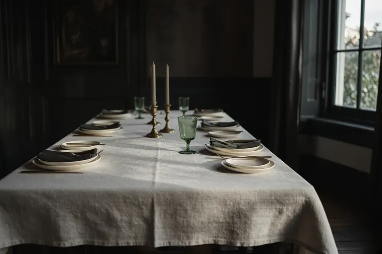 A long empty table set for a meal, linen, brass and a green glass.