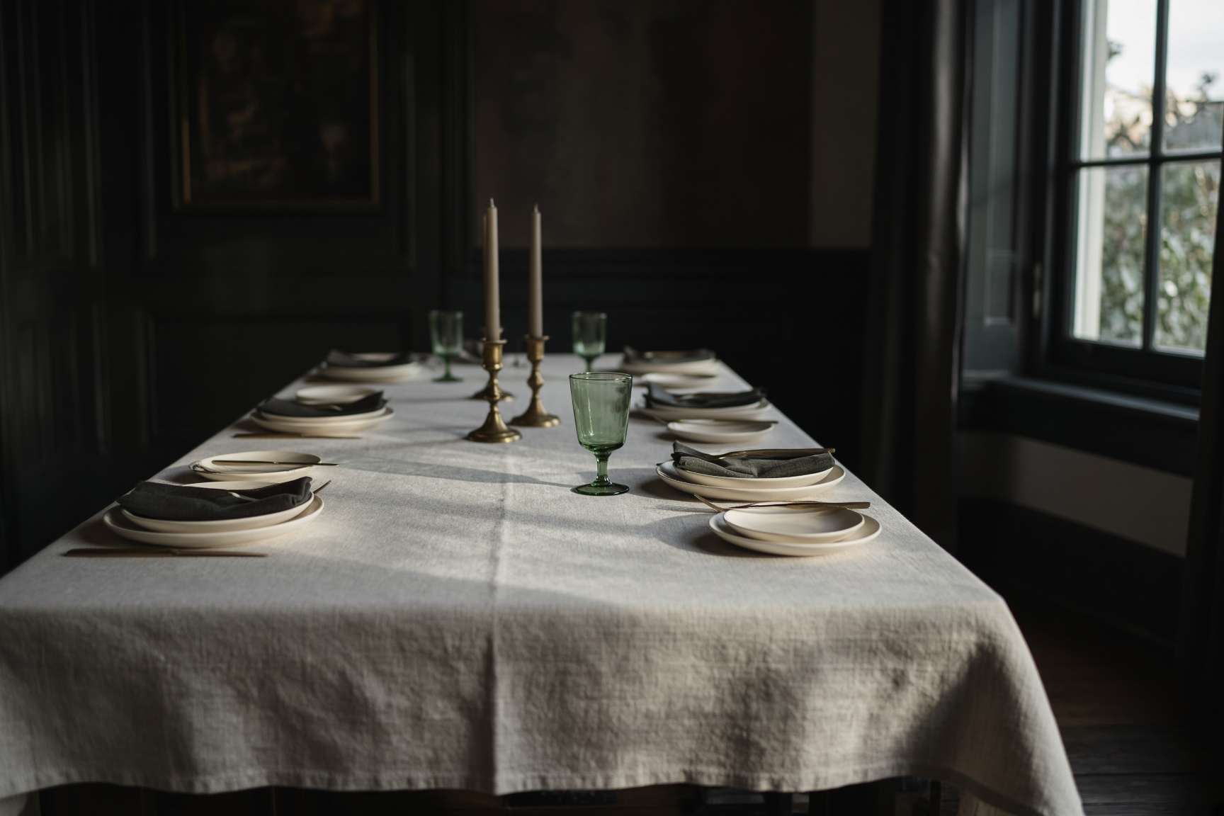 A long empty table set for a meal, linen, brass and a green glass.